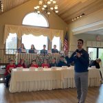 Students sitting at table while a person speaks into mic at the Mechanicville CSD 2nd Annual Educator P2 Summit