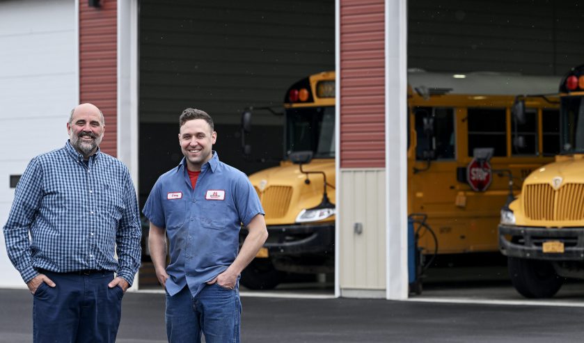two smiling staff members in front of bus garage