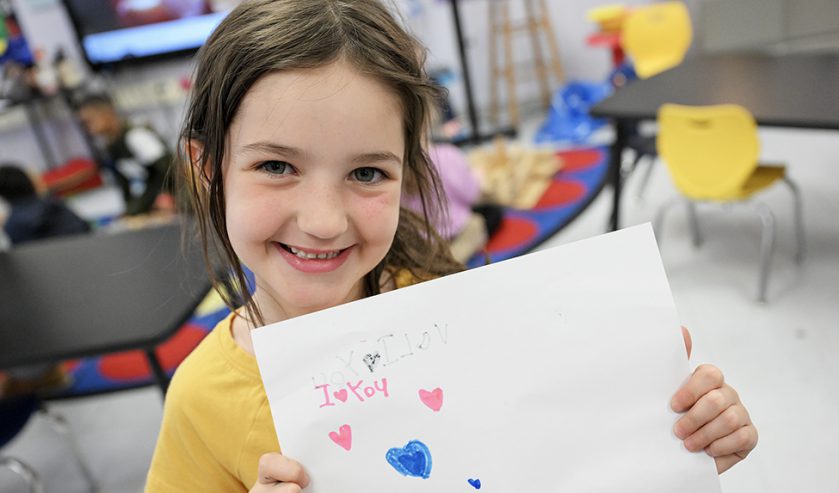 An elementary student holding a paper that says I love you