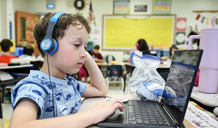 An elementary student at desk looking at a laptop screen.