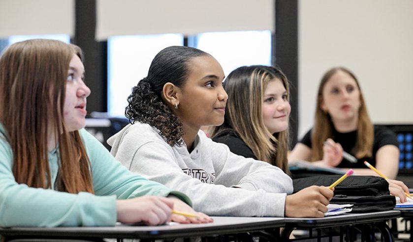 4 students in classroom at desks listening.