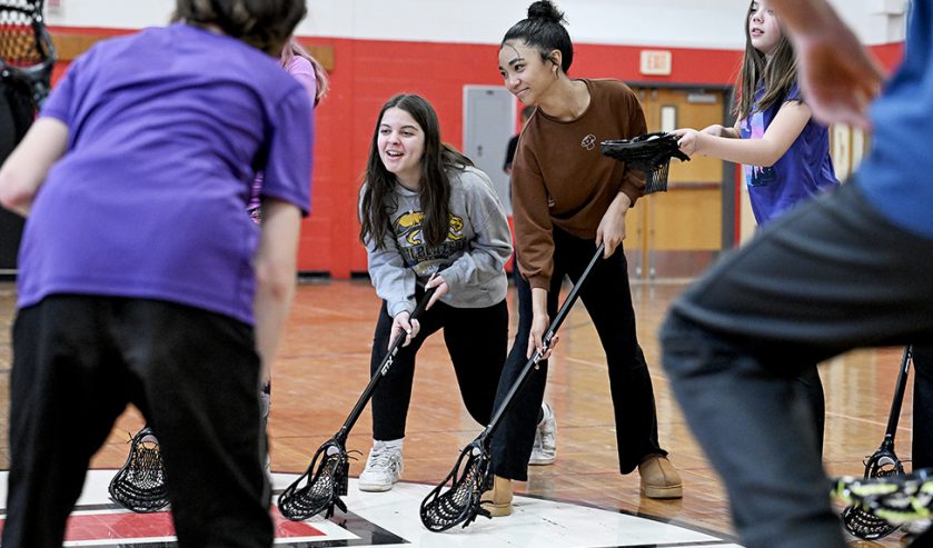 6 students in gym with lacrosse sticks